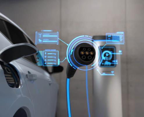 Im Bild wird die Ladeinfrastruktur für E-Fahrzeuge gezeigt: Im Hintergrund ist eine Ladestation, ein Ende des Ladekabels zeigt direkt in die Richtung des Betrachters.