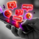 Eine Hand hält ein Handy, über dessen Oberfläche Icons schweben, die digitale Gewalt darstelllen